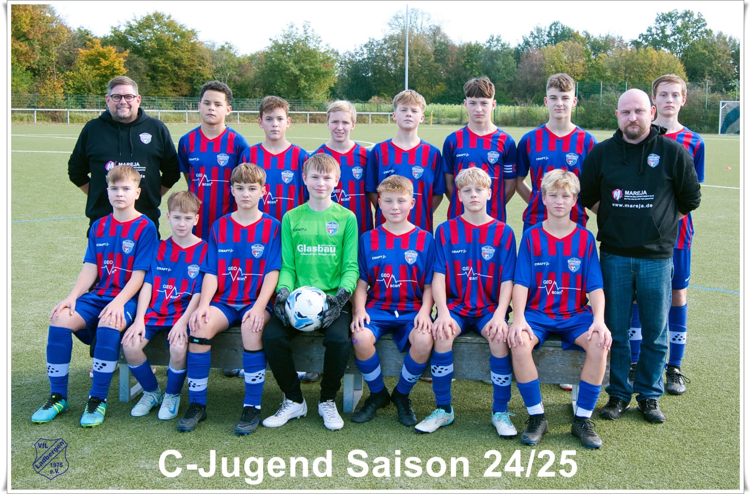 Jugend-Fußballteam in blau-roten Trikots mit zwei Trainern, ernste Gesichtsausdrücke.